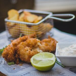 Close-up of fried fish and chips with tartar sauce and lime, perfect for food lovers.