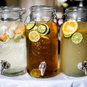 Close-up of citrus-infused drinks in stylish glass jars with tap dispensers, perfect for summer refreshment.
